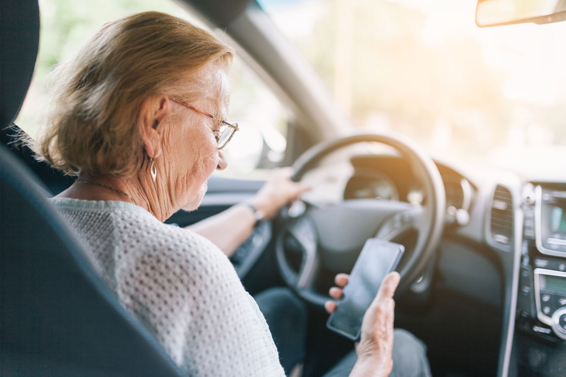 Elderly woman behind the steering wheel of a car using her phone